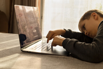 A 10-year-old boy studies online and falls asleep from fatigue or laziness in front of a laptop