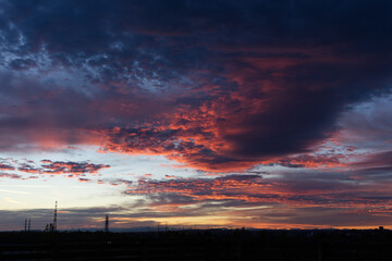 Fototapeta premium Colorful sunrise with heavy clouds with small power lines silhouettes on the horizon