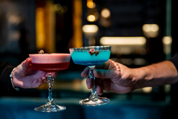 man and woman hand clinking glasses of alcoholic cocktails in bar