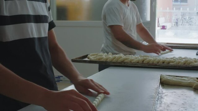 Two male bakers in a bakery make synchronized movements, forming dough