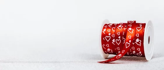 Fotobehang A roll of red gift ribbon with printed hearts for St Valentines day or 14 February. Minimal wide banner with copy space © taniasv