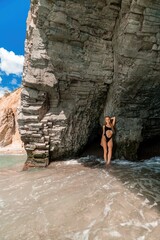 Woman swimsuit sea. Attractive blonde woman in a black swimsuit enjoying the sea air on the seashore around the rocks. Travel and vacation concept.