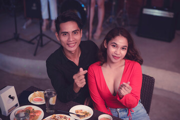 A loving boyfriend and girlfriend smile at the camera and pose with a finger heart. Successful couple matchmaking. Successful first date.