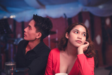 A couple having a date at an elegant restaurant sits back to back and ignores each other as they are having an argument. A lady is upset with her insensitive boyfriend. Waiting for the night to end. - obrazy, fototapety, plakaty
