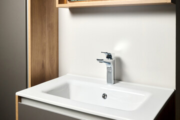 Interior of bathroom with washbasin mirror cabinet over the sink and faucet modern loft flat minimalistic design with modern countertop basin, illuminated mirror and wooden PVC cupboard.
