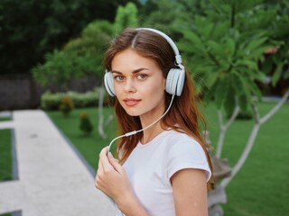 Woman portrait in headphones in a white T-shirt listening to music and walking down the street, smiling, with palm trees in the background