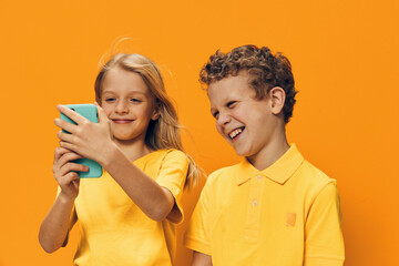 happy, joyful children are standing on a bright orange background and smiling holding a phone in their hands, smiling cheerfully