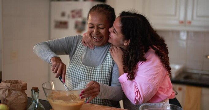African mother and daughter having tender moment while preparing fruit cake at home - Family and cooking concept