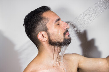 Water pours on the guy's face on a white background. The concept of taking a shower and washing your head.