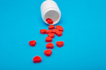 Red heart shaped pills with plastic bottle on blue background.Concept love addiction, love drugs, Valentine's Day and depression