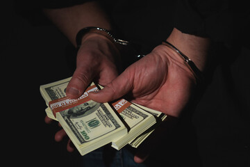 Close up arrested man holding money in handcuffs against black background as a symbol of...