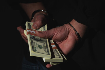Close up arrested man holding money in handcuffs as a symbol of corruption, illegal gratuities....