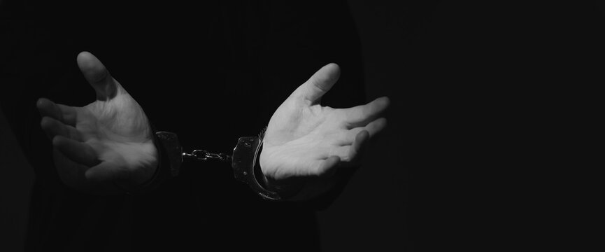 Arrested man in handcuffs as a symbol of сrime and destructive antisocial behavior. Black and white image. Copy space.
