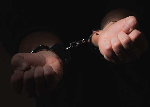 Close up arrested man in handcuffs as a symbol of сrime and destructive antisocial behavior. Selective focus on hands.