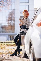 Woman charging electric car and using phone