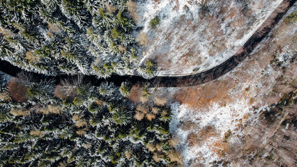 Aerial high angle view of narrow winding curvy mountain road among the trees covered with snow in winter forest. Snowy landscape, view from above.
