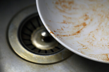 Dirty white plate covered with some ketchup. Placed to a sink for getting washed. Closeup color image.