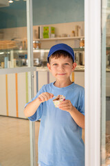 Сute 6-year-old boy in a blue T-shirt eats ice cream (gelato) with a spoon from a glass in a gelateria in Rome. Traditional dessert, tourism with children.