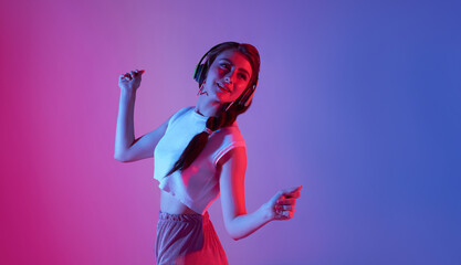 Happy beautiful teen woman listening music and dance on neon background.