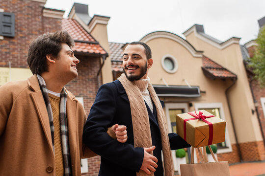 Bearded Gay Man With Shopping Bag And Christmas Present Looking At Young Boyfriend On Urban Street.