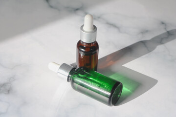 Green and brown bottle facial essential oil or serum packaging on white marble background. Beauty cosmetic product for skincare concept. minimal and luxury style. Light and shadow.