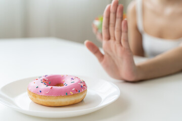 Woman on dieting for good health concept. Close up female using hand push out her favourite donut and choose green apple and vegetables for good health.