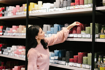 A young brunette woman in a pink sweater buys a decorative candle in a store.