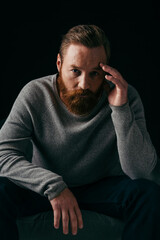 Obraz premium Portrait of bearded man looking at camera near armchair isolated on black.