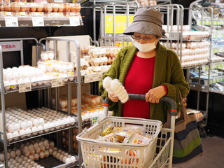 スーパーのたまご売り場で買い物する高齢日本人女性