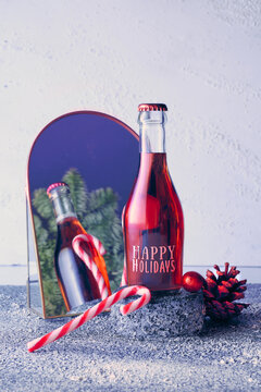 Small bottle of rose, pink vine on stone pedestal reflected in arc mirror. Christmas, wintertime celebration concept. Xmas wintertime decor with candy canes, pine cone and fir twig on off white