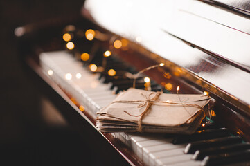 Paper snail mail letters in laced envelope on piano keys over glow Christmas lights close up....
