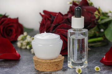 Fototapeta na wymiar Natural, homemade face cream and face serum. Rose face moisturizer and rose water on grey marble background with red roses. 