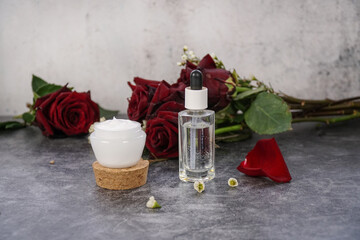                       Natural, homemade face cream and face serum. Rose face moisturizer and rose water on grey marble background with red roses.       