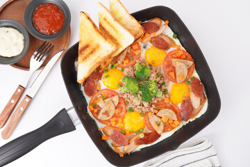 Fast food breakfast, fried eggs in pan and vegetables, top view.