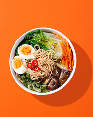 Ramen noodle soup with eggs, mushrooms, pak choi in hard light on orange