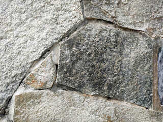 Granite stone wall surface. These stones have been joined together using mortar. The construction of this wall requires precision so that it can be built upright with an almost flat surface.
