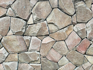 Granite stone wall surface. These stones have been joined together using mortar. The construction of this wall requires precision so that it can be built upright with an almost flat surface.
