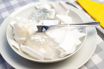 Laid table, with white plates and glass containing plastic waste. Plastic in the environment and microplastics in food. 
