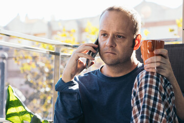 young man calling on the phone and drinking tea or herbal tea on the terrace of his house