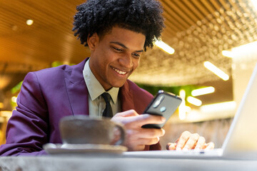 Elegant happy black man using smartphone while texting message at table