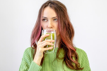 Woman Drinks Matcha. A beautiful girl in a green sweater holds matcha tea in her hand in a transparent cup against a white background.