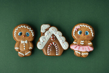 Christmas gingerbread house shaped cookies with white snow icing on a green background. Homemade festive traditional gingerbread cookies. Merry Christmas greeting. Gingerbread couple