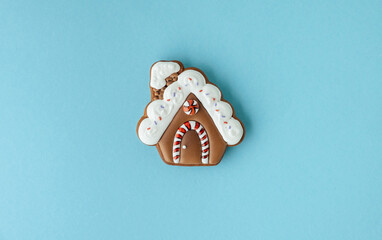 Christmas gingerbread house shaped cookie with white snow icing on a blue pastel. Homemade festive traditional cookies. Merry Christmas greeting