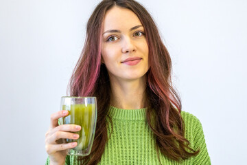 Smiling woman in a good mood drinking matcha A beautiful girl in a green sweater holds a cup of hot matcha tea in her hand in a clear glass.