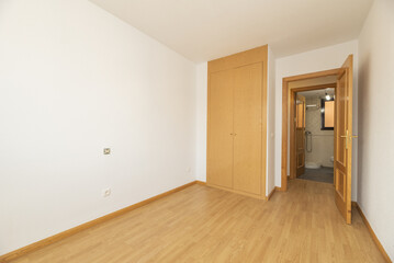 Empty room with oak colored wooden built-in wardrobe with matching flooring and plain white walls