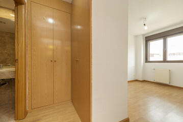 Empty room with oak-colored wooden built-in wardrobes with a matching floor forming a walk-in closet and access to a bathroom with a marble countertop