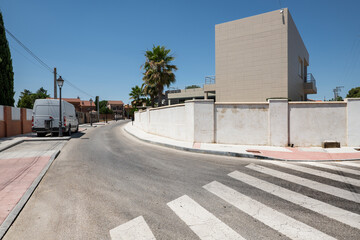 A street in an urbanization with a curved zebra crossing and palm trees
