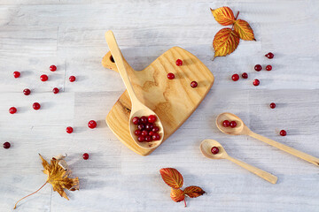 Fototapeta na wymiar Wooden spoon filled with ripe cranberries on a wooden cutting board, the berries are scattered among the spoons on a light background, top view
