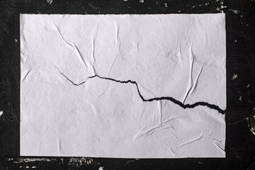 Paper with folds and a crack on a black wall.