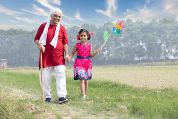 Happy grandfather with cute little girl running carefree and having fun with colorful pin wheel.